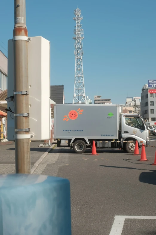 a street in front of a television tower, with traffic cones on the side of the road