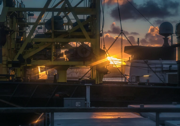 the sun rises behind a dock with industrial machinery