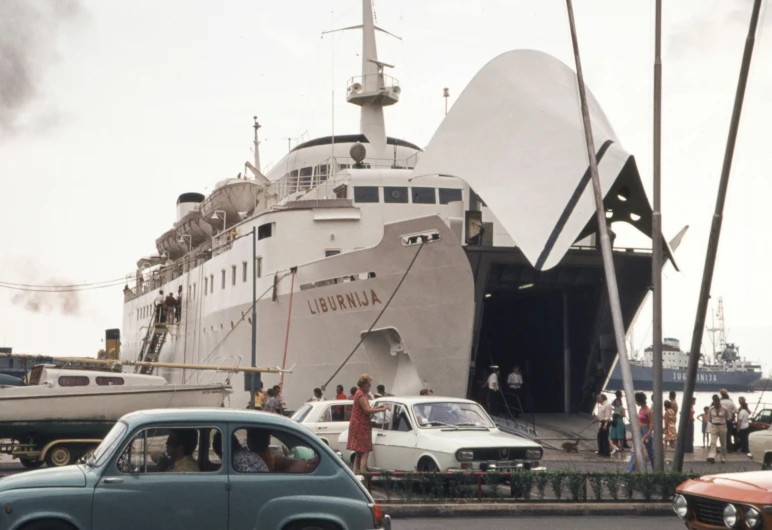 a car waiting in front of a boat with people on board