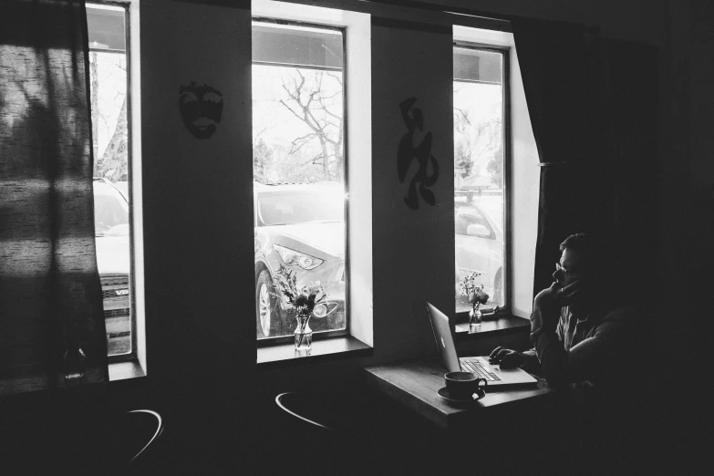 a woman sits at a computer next to two windows