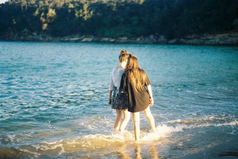 two women standing on the shore next to a body of water