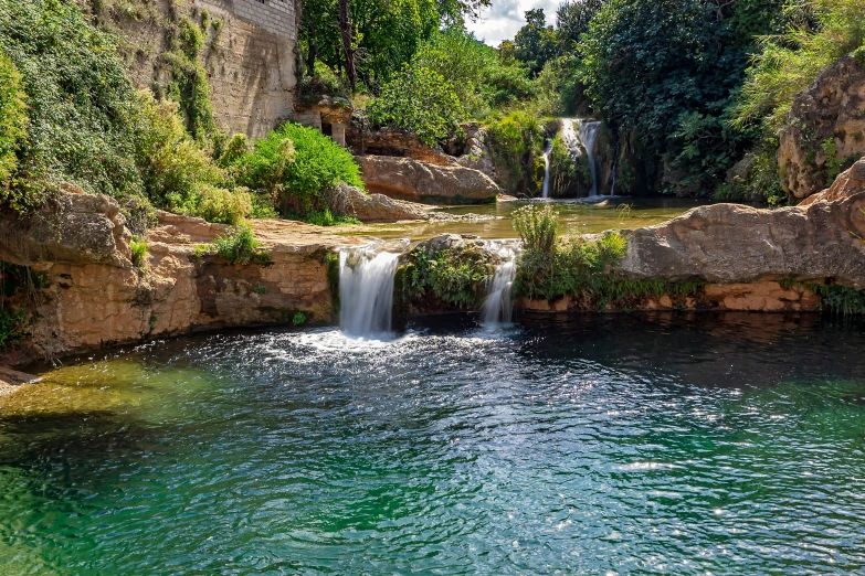 a waterfall in the middle of a pool surrounded by lush green trees