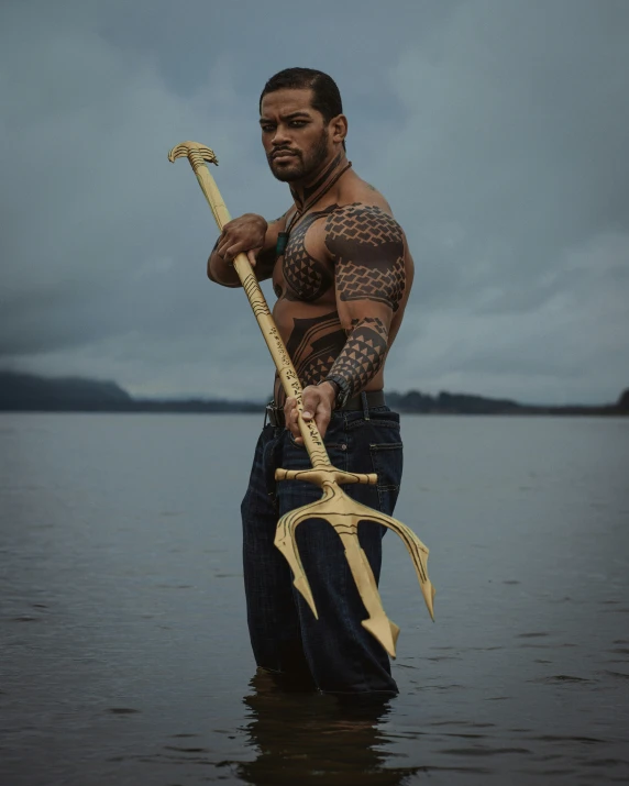 a man with tattoo standing in a body of water holding an axe