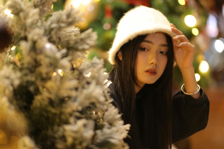 young woman wearing a white hat near a christmas tree