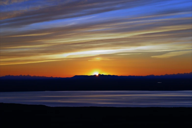 a cloudy sunset reflects the sun in the distance over a body of water