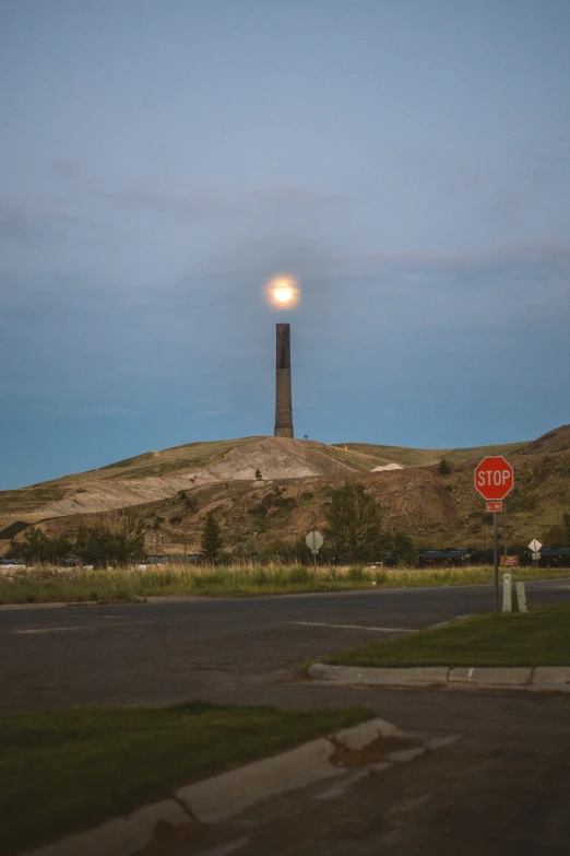 a stop sign at the top of a hill with a light tower above it