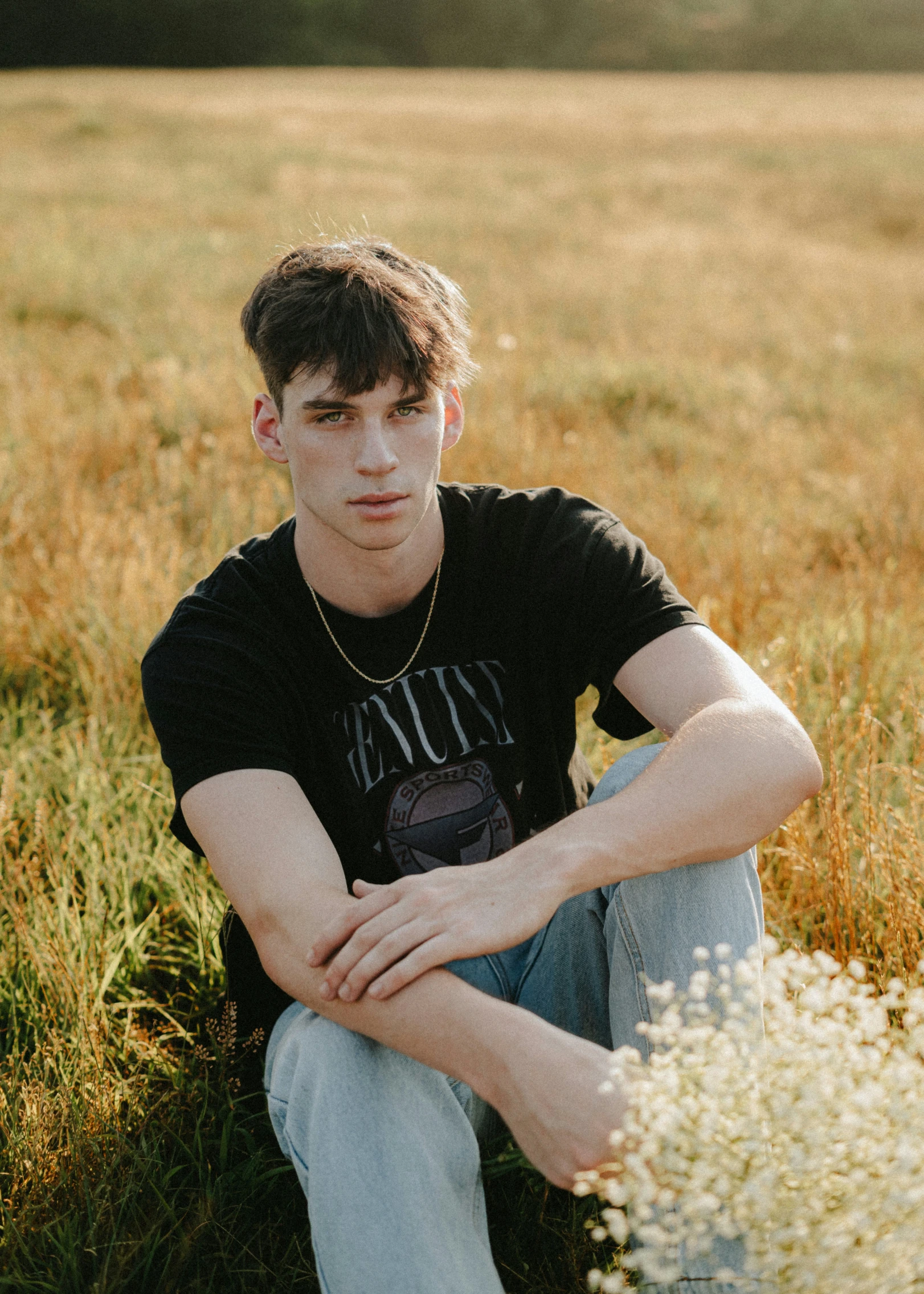 a young man with his legs crossed sitting in the middle of a field