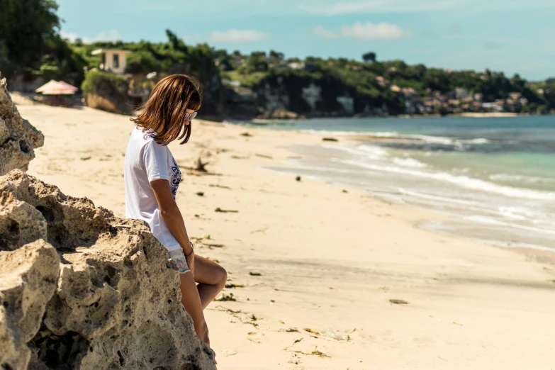 a woman sitting on the rocks of a sandy beach