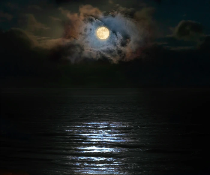 the full moon is visible in the dark cloudy sky above the water