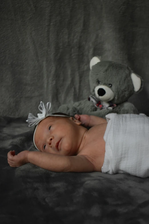 the small baby in white is laying down beside a stuffed teddy bear