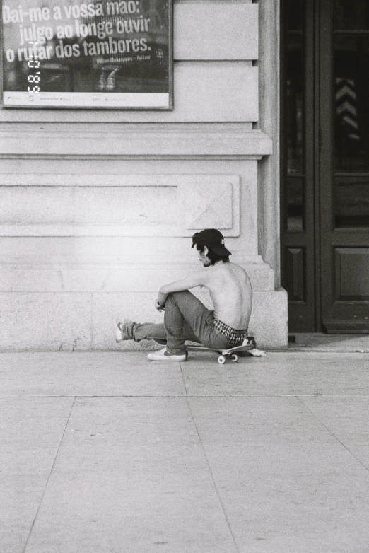 black and white pograph of person sitting on curb with foot over sidewalk