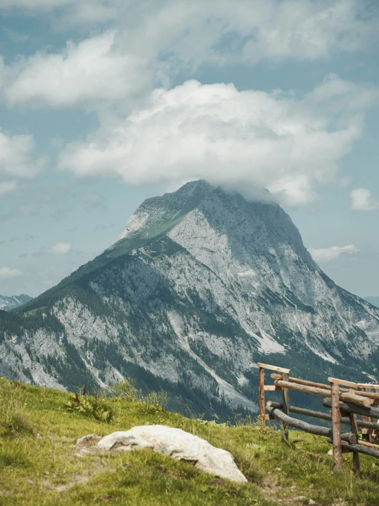 a wooden bench is on the top of a hill with grass and mountains