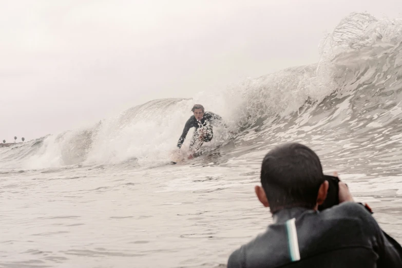 a man surfing next to a surfer as he looks at a wave