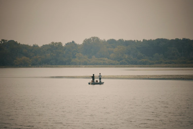 three people fishing in a calm lake in the day