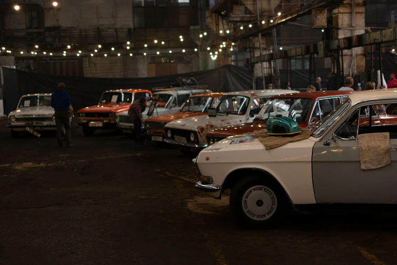 a line of cars parked on a street with people near by