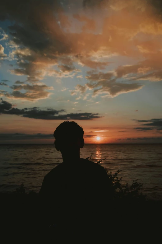 man looking at ocean against colorful sky with sun low to ground