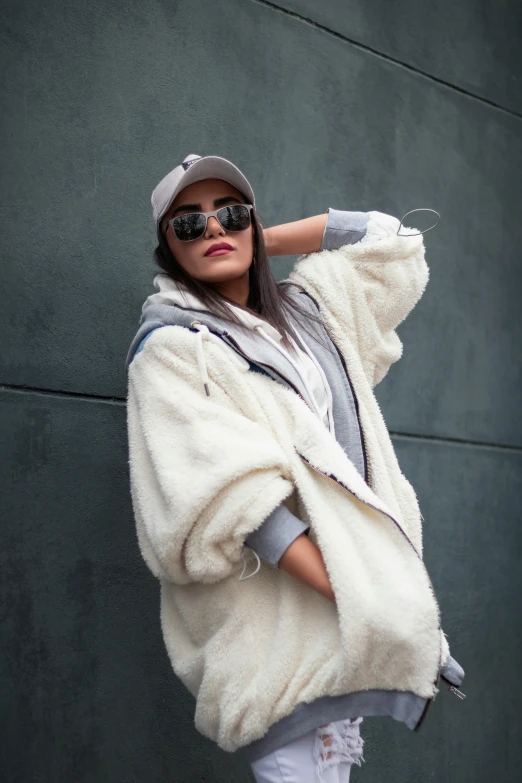 a young lady standing against a wall wearing a white jacket