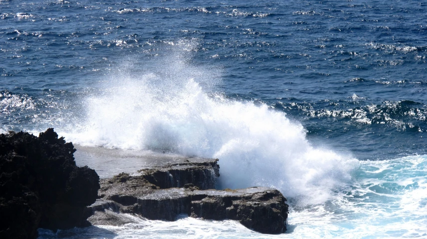 a bird flies low over a rock out on the water