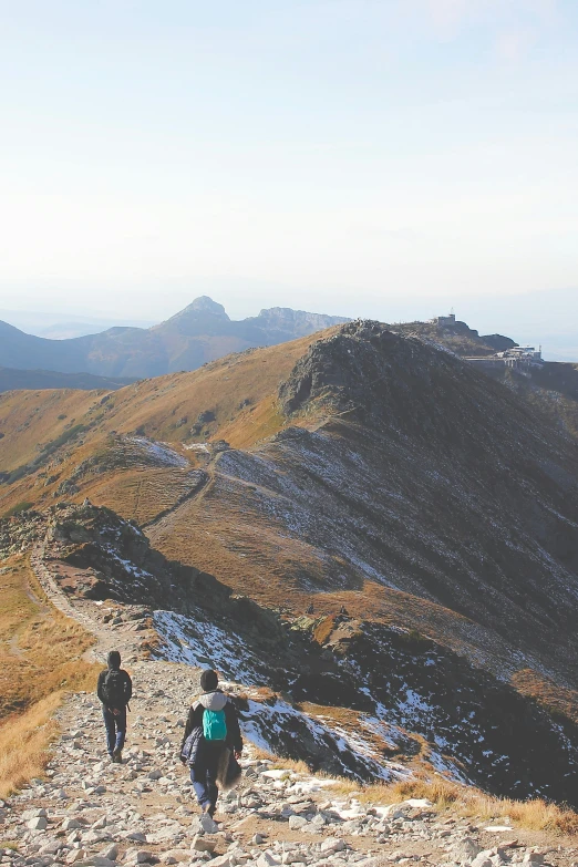 two people with backpacks walk down a path on a hill