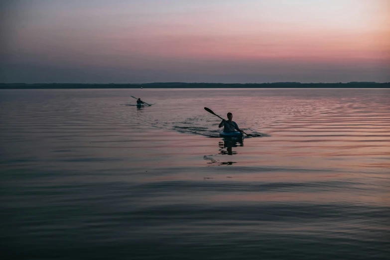 a couple paddle boarding in the open water at sunset