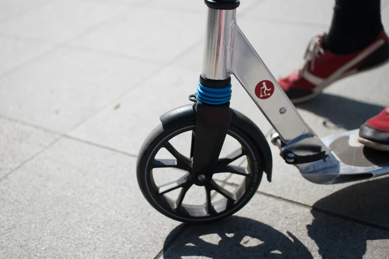 a closeup of a scooter wheel with someone walking in the background