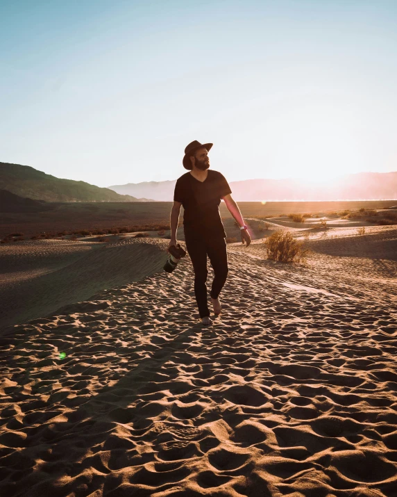 a man carrying surfboards along the beach at sunset