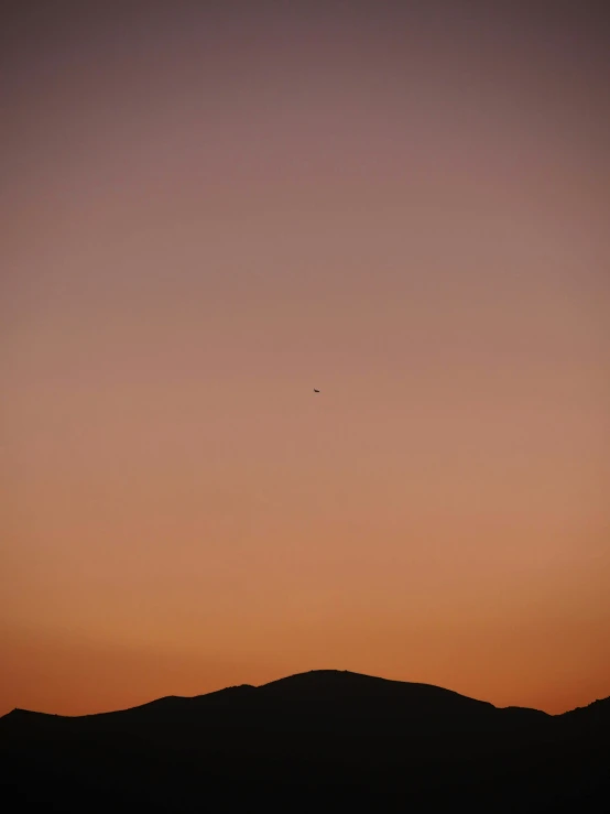 a lone plane is flying over a mountain at sunset