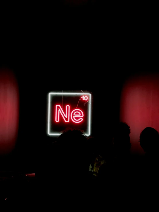 a neon sign is in the dark with people behind it