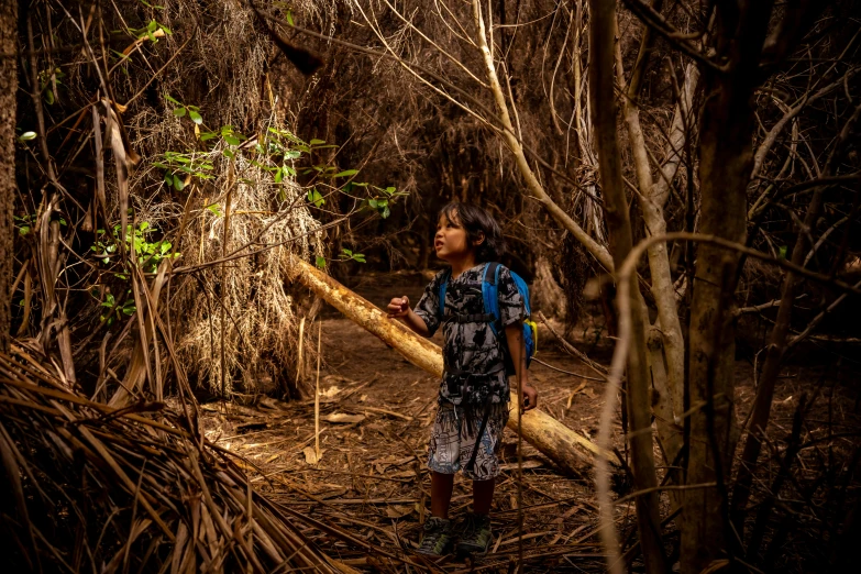 a young person stands in a thicket holding a log