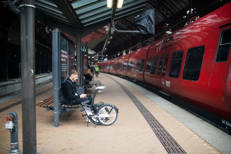 a lady sitting next to her bike in front of a train station