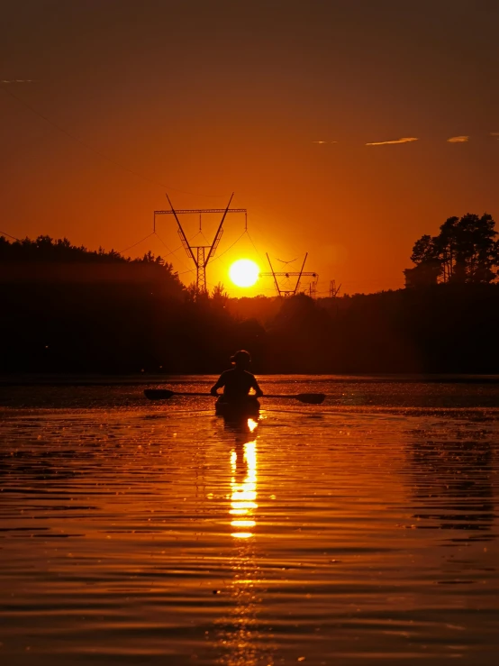 a silhouette of a person on a boat under the setting sun
