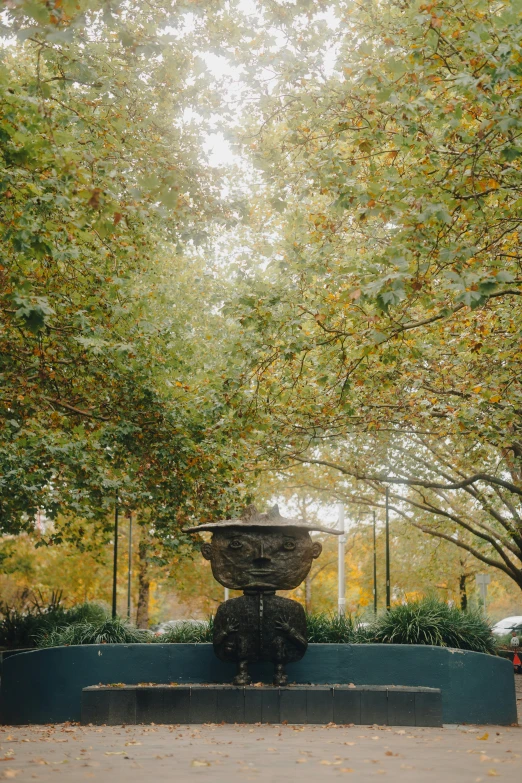 a fountain in the middle of a park with trees lining it