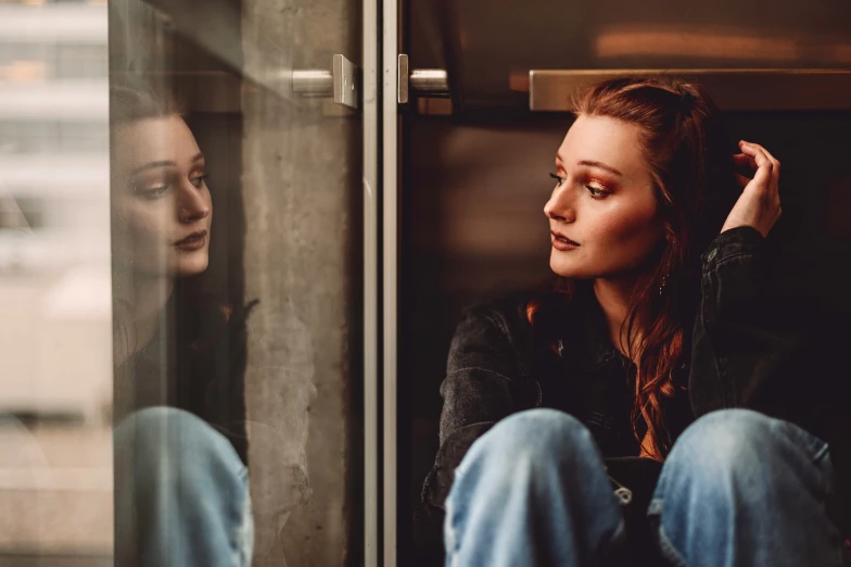 two women are sitting against a window and one is staring outside