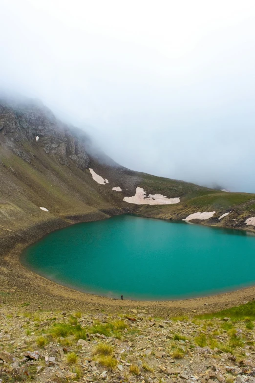 the mist rolling on top of a green mountain and blue water