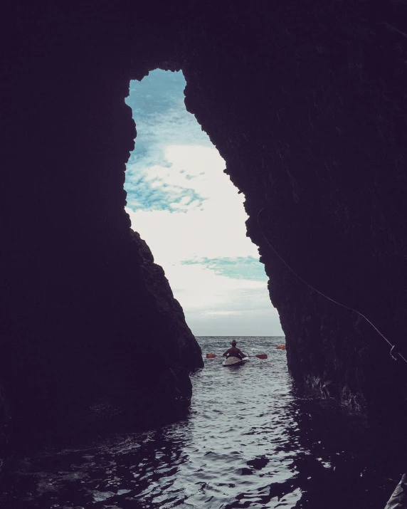 the silhouette of a person in a kayak in a large cave