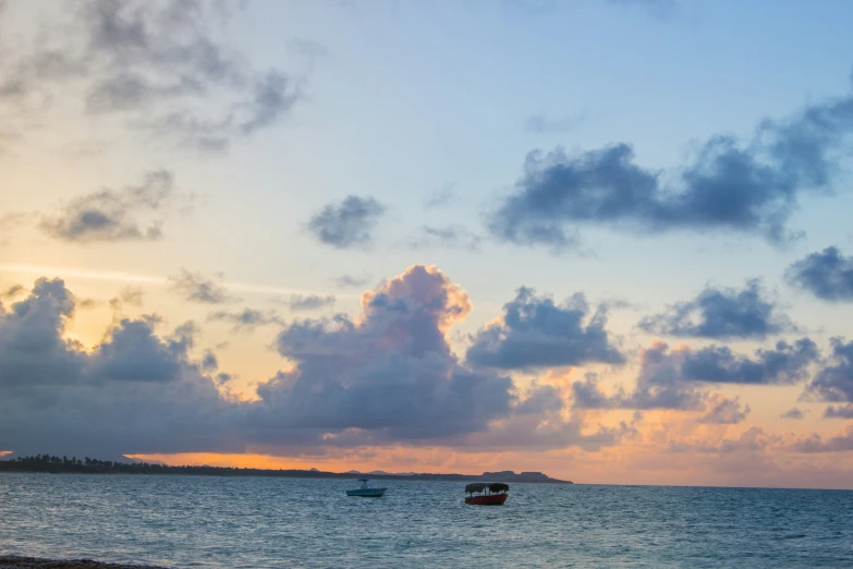 a beach with small boats out in the water at sunset