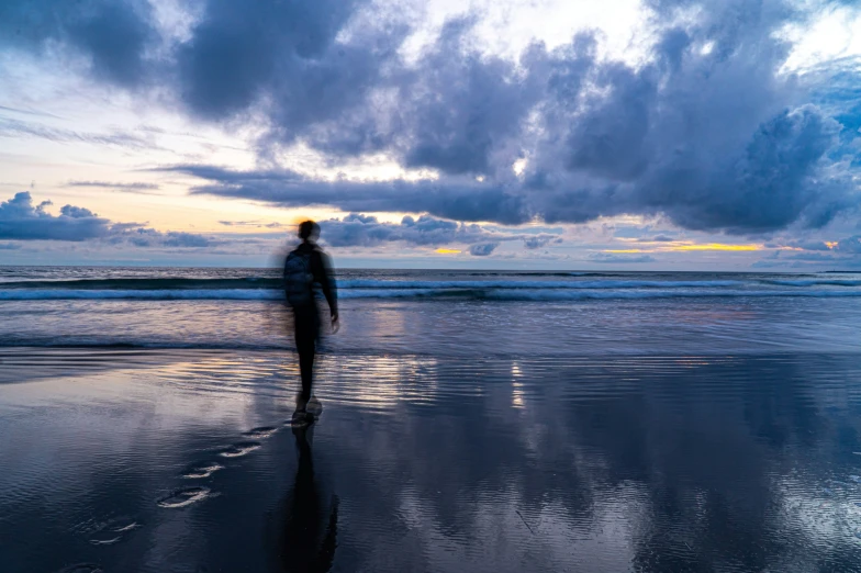 a man walking along the beach under dark clouds