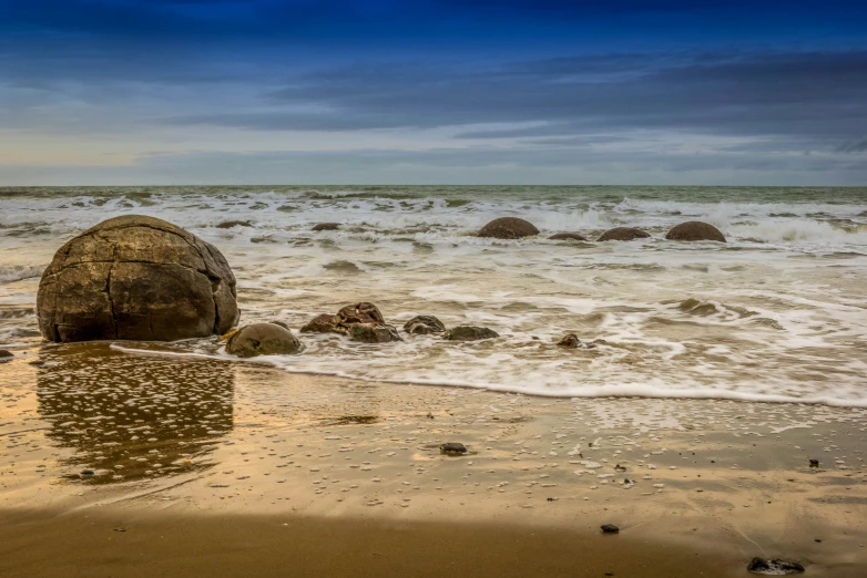 a wave splashing in on the beach while a rock sits on the sand