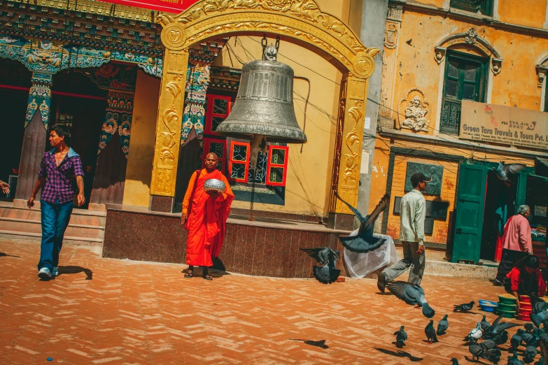 several people walk around a small plaza with a bell on it