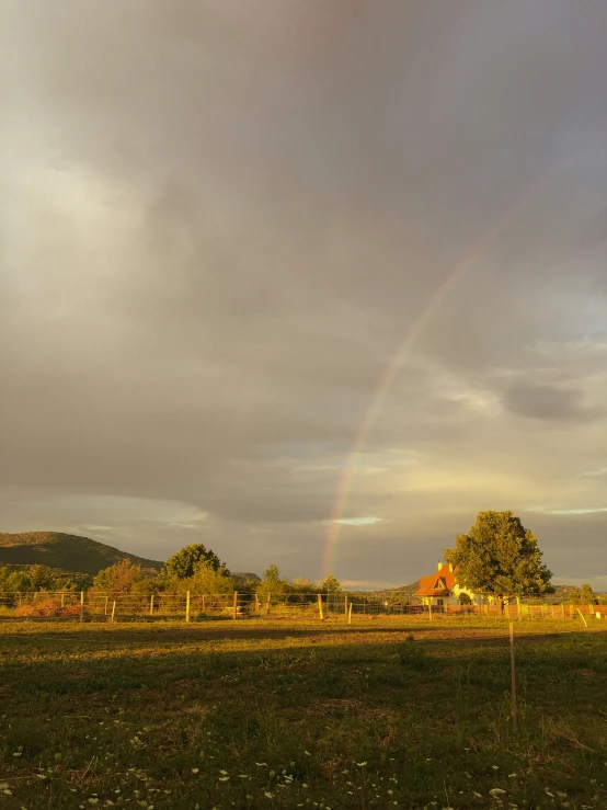 a house under an rainbow with a dirt road and fence