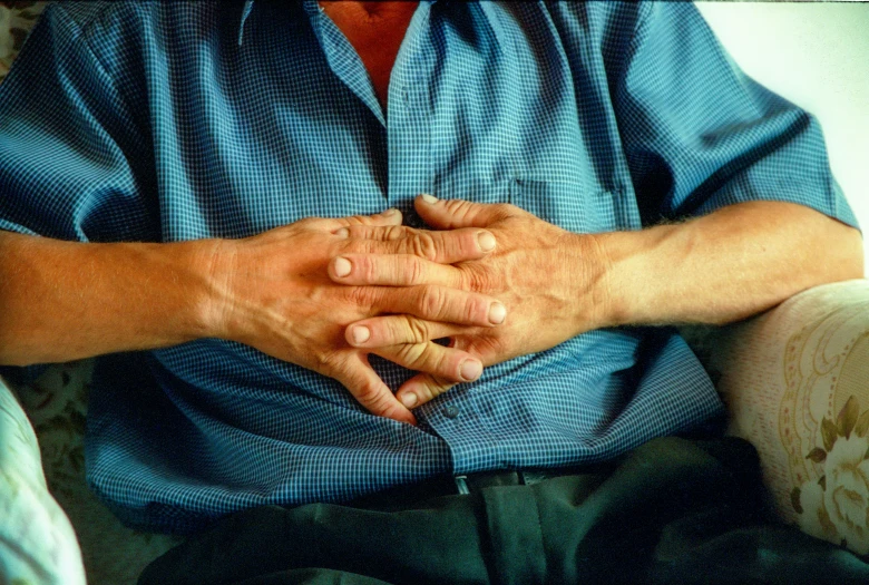 an old person sitting on a couch with his hands together