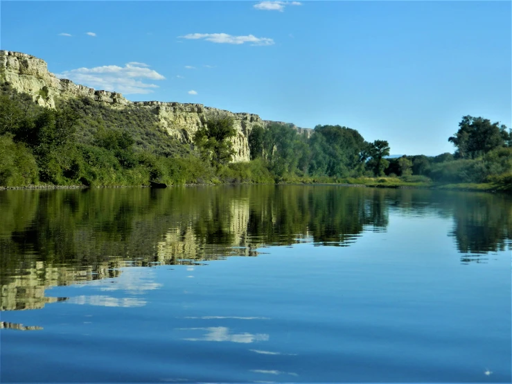 trees are reflected in the water while the cliff walls are covered by trees