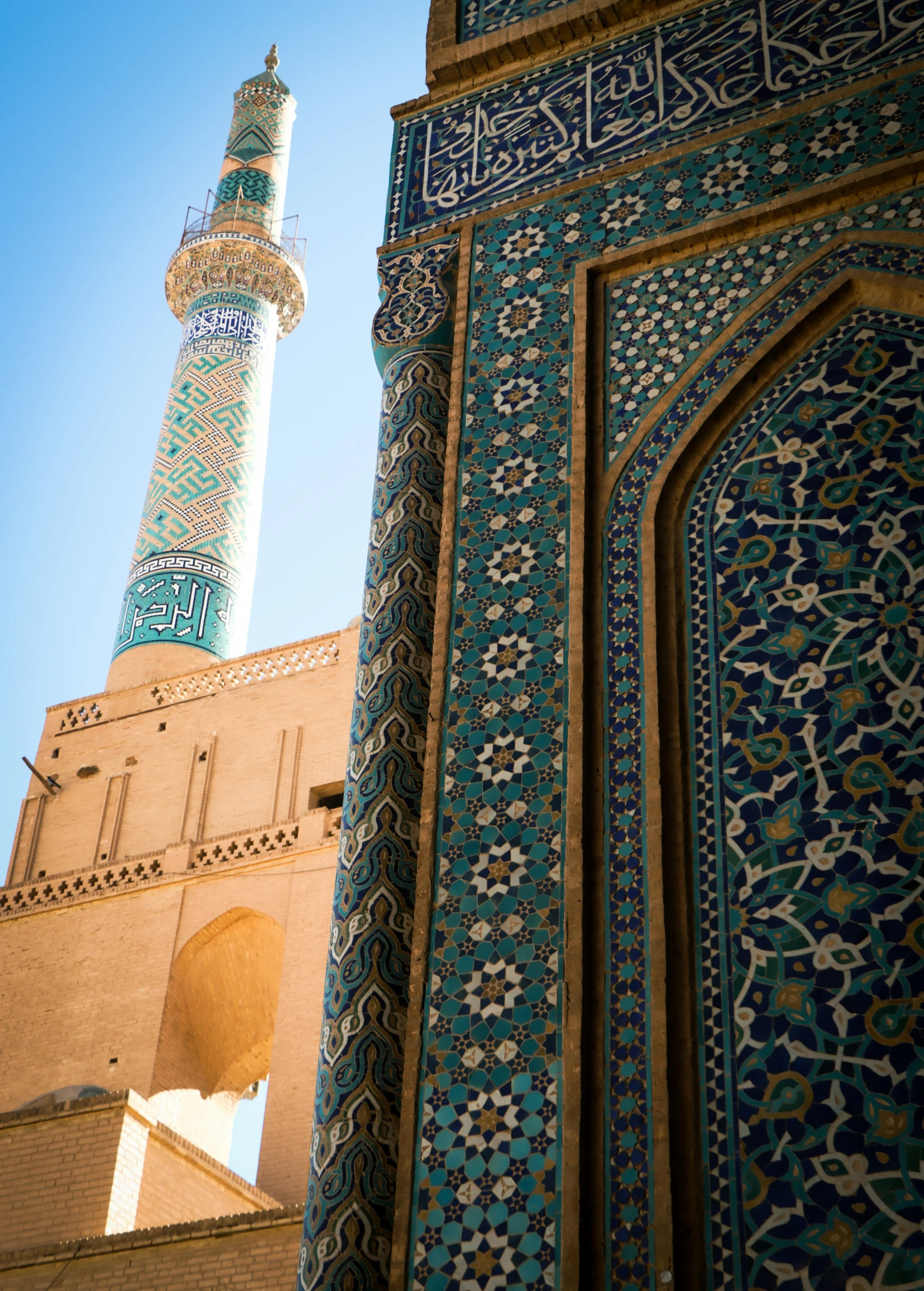 looking up at the minaret of a building, featuring decorative tilework and a cross - work on one side