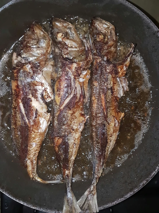 fish being cooked in a black pan on the stove