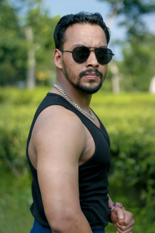 a man with a short black top wearing shades standing in a field