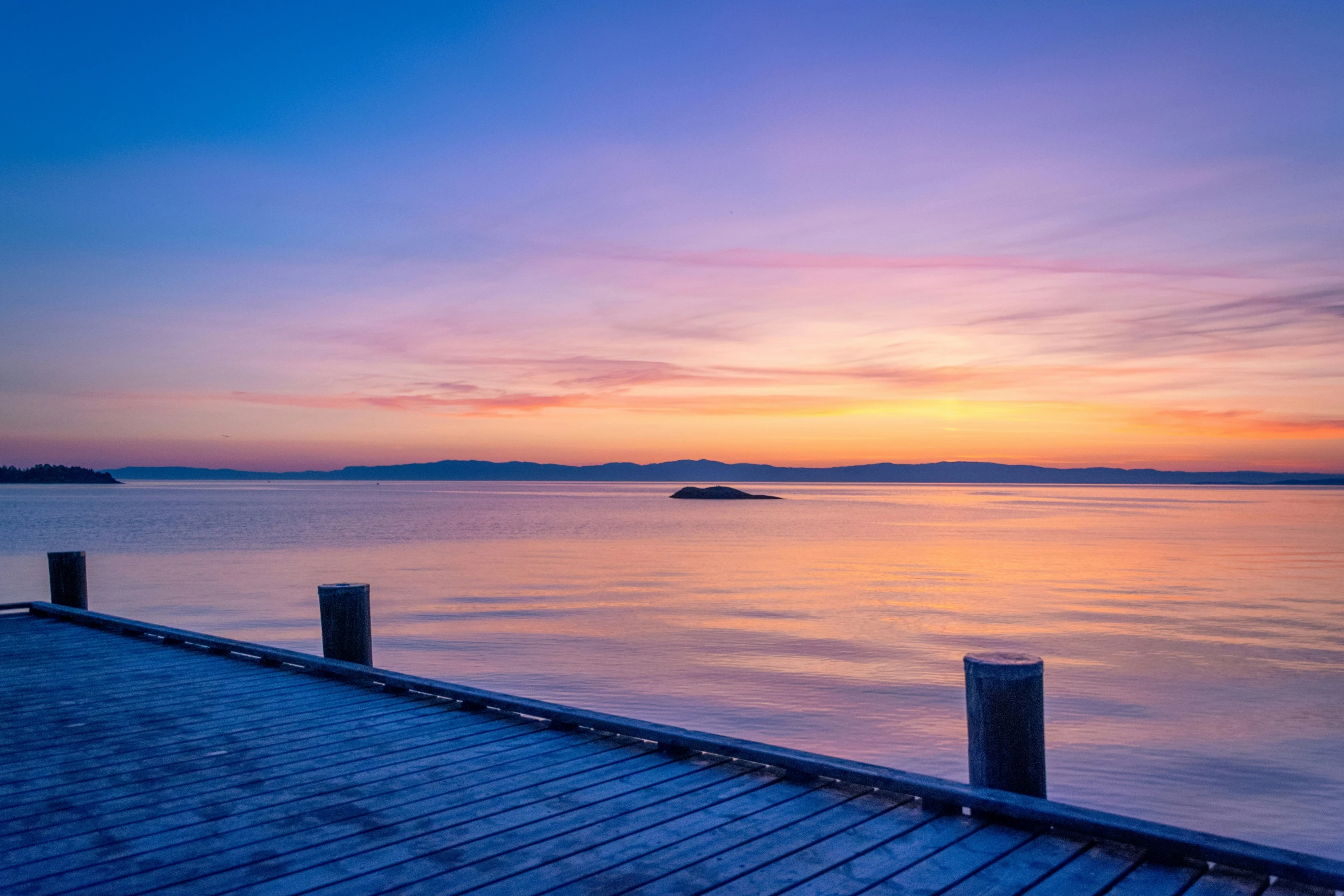 a dock sitting on the side of a body of water under a colorful sky