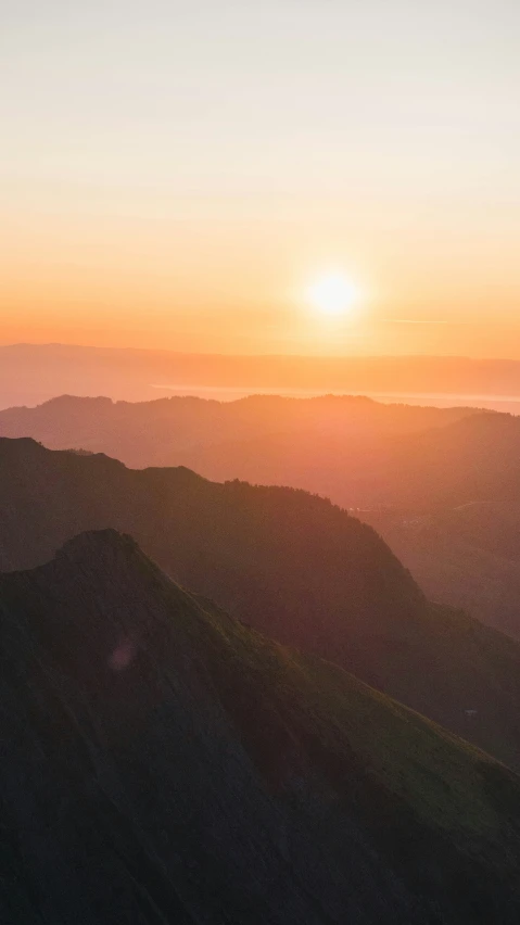 a view of some hills with the sun setting in the distance