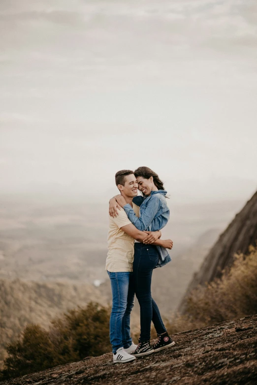 two young people hugging each other on top of a mountain