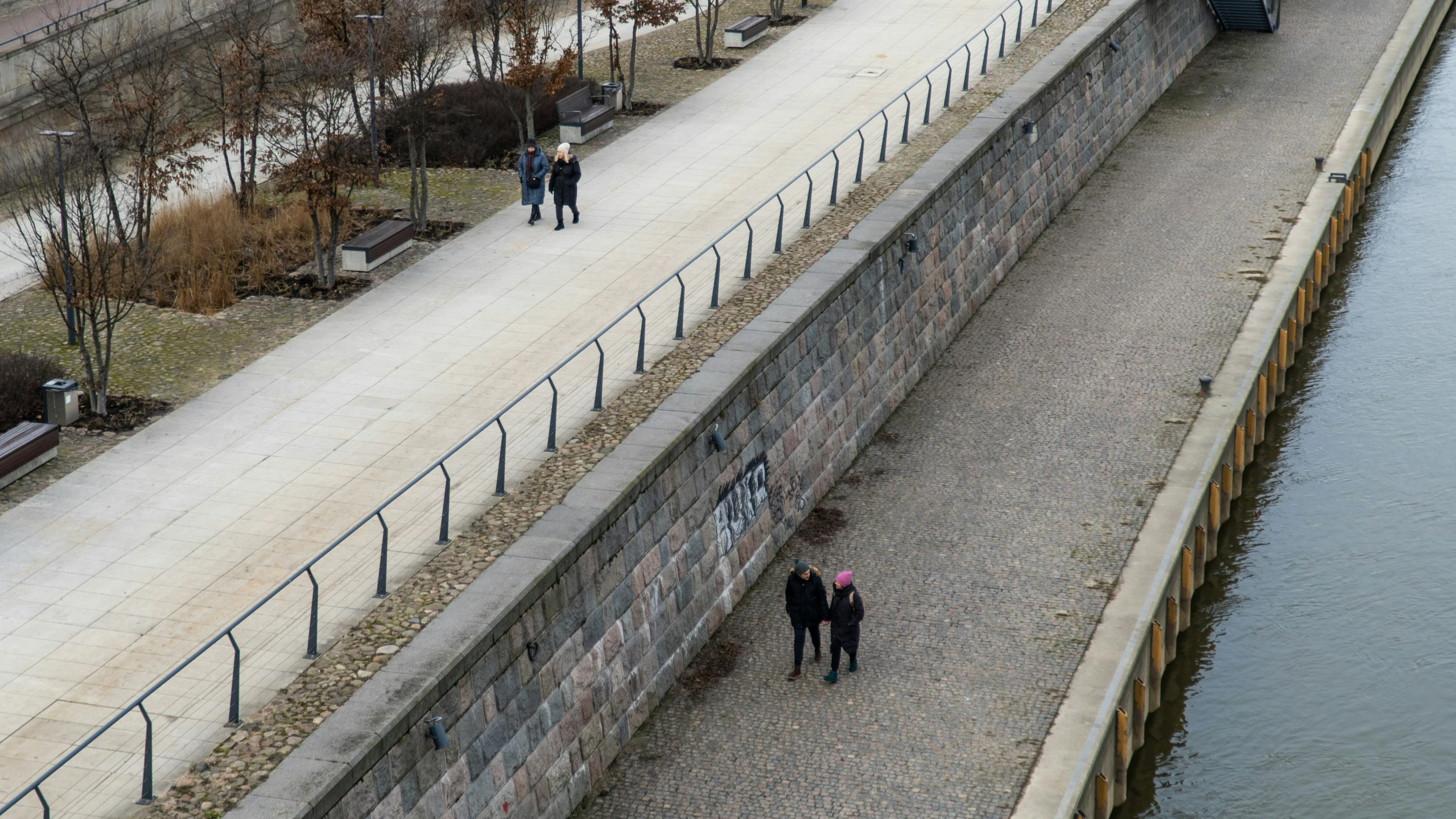 a couple of people are walking by a wall next to a body of water