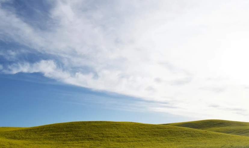 a big grassy field sitting under a cloudy blue sky